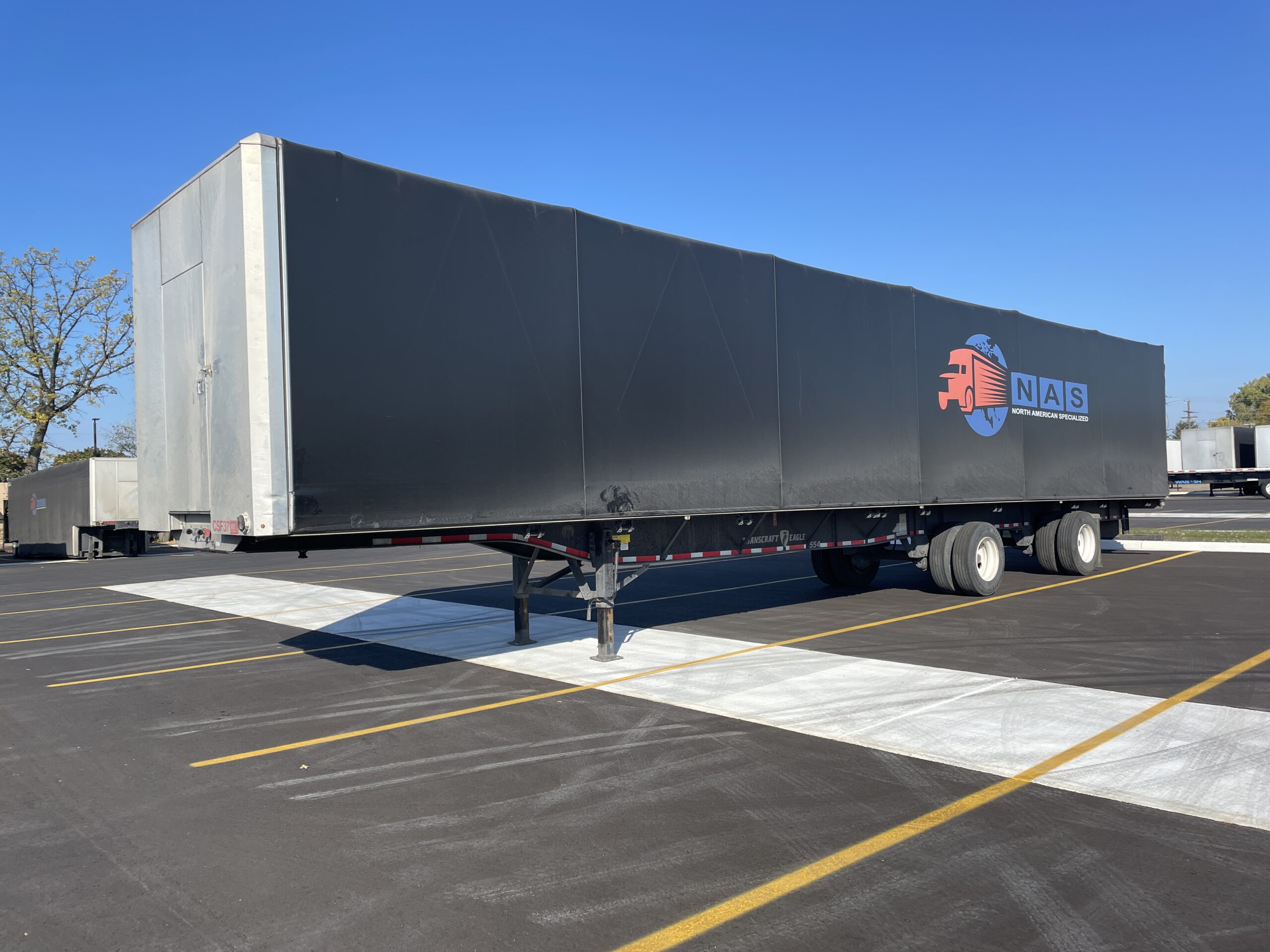 Black NAS truck trailer parked in empty lot under clear blue sky