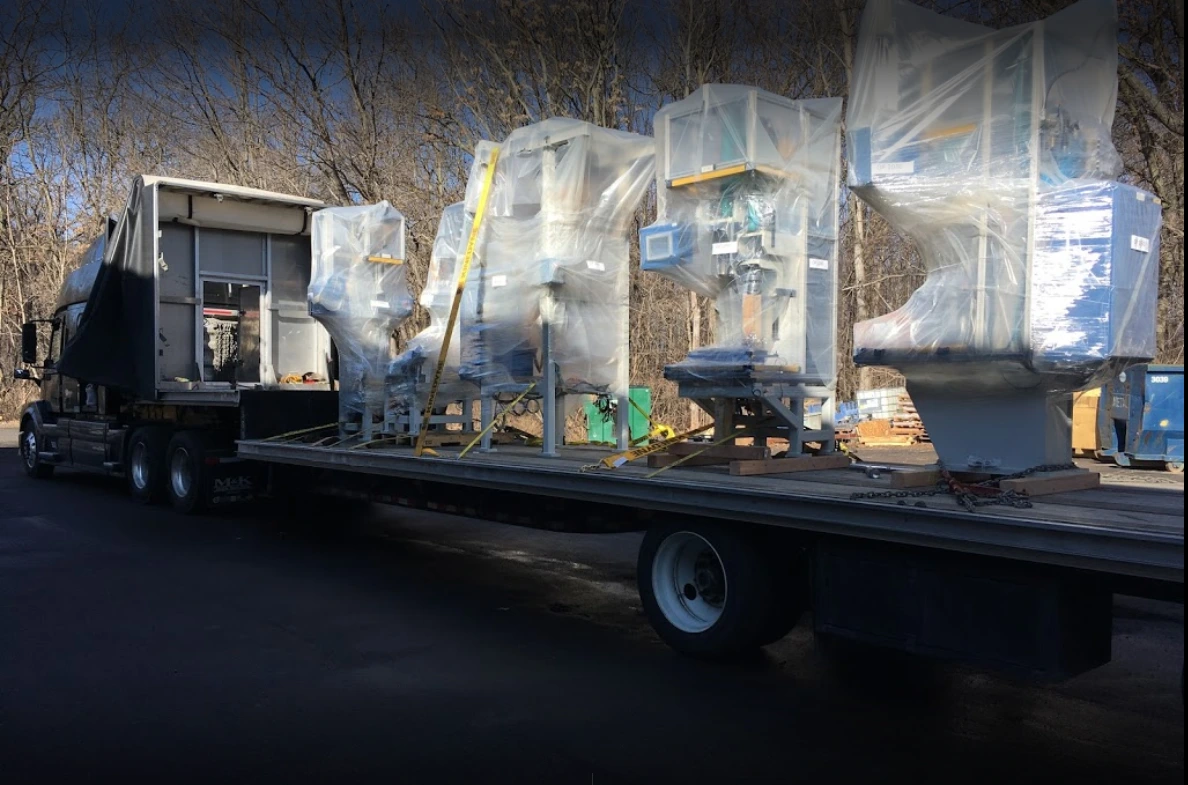 Flatbed truck carrying wrapped industrial equipment on a sunny day.