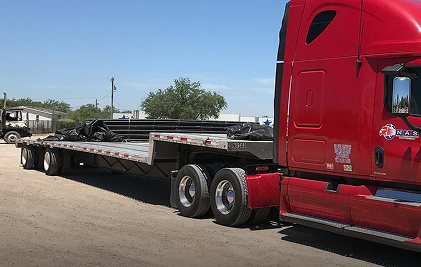 Red semi-truck with flatbed trailer parked on gravel in industrial area.