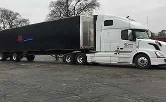 White semi-truck with black trailer parked on asphalt, trees in background.