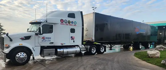 White semi-truck with decorated trailer parked on wet pavement under cloudy sky.
