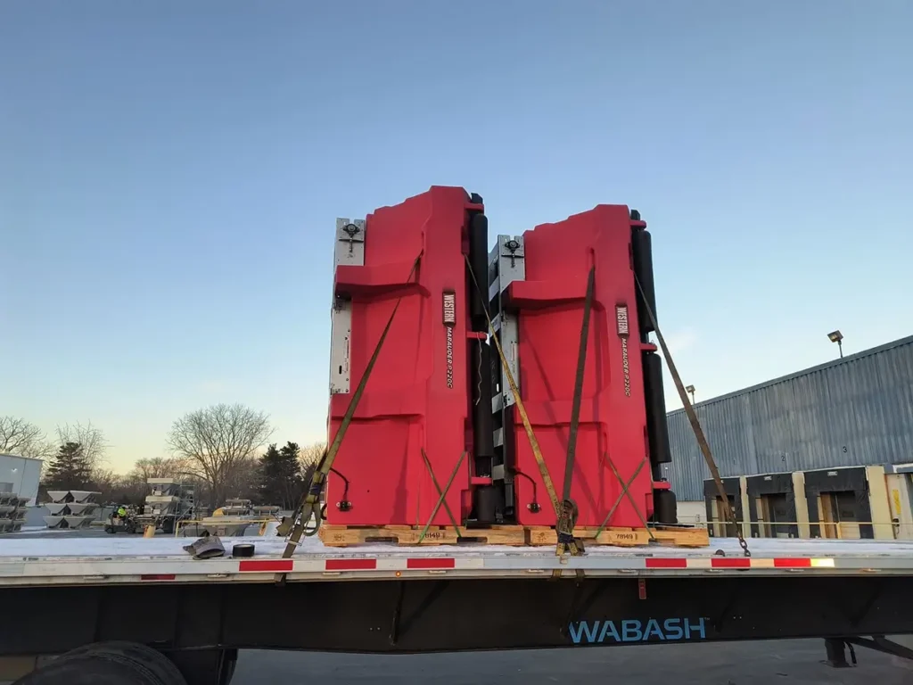 Two large red machines secured on a flatbed truck against a clear sky at an industrial site.